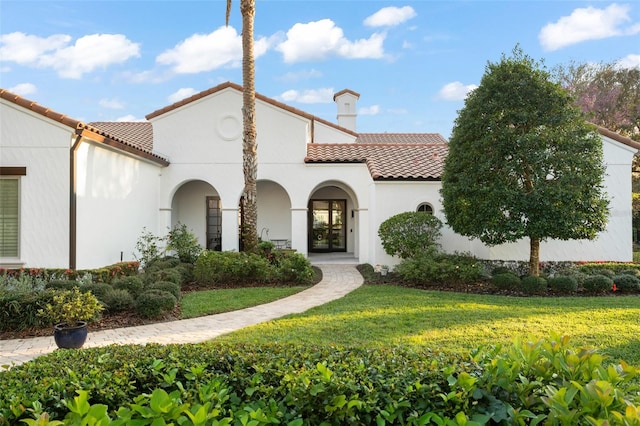 mediterranean / spanish-style house featuring a front yard, a tile roof, a chimney, and stucco siding