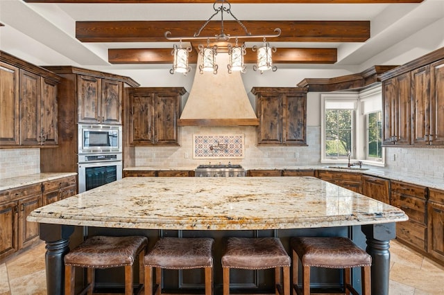 kitchen with a center island, beam ceiling, a breakfast bar, appliances with stainless steel finishes, and a sink