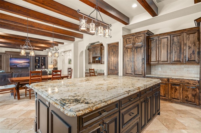 kitchen with arched walkways, hanging light fixtures, backsplash, a kitchen island, and light stone countertops