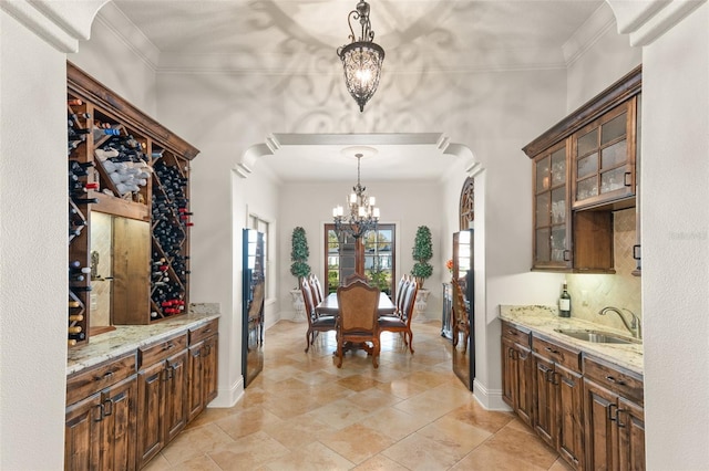 interior space with crown molding, a notable chandelier, glass insert cabinets, a sink, and light stone countertops