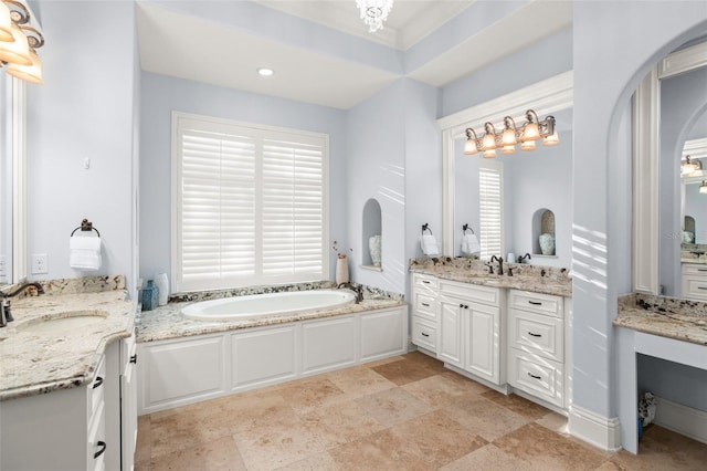 bathroom featuring a garden tub, two vanities, and a sink