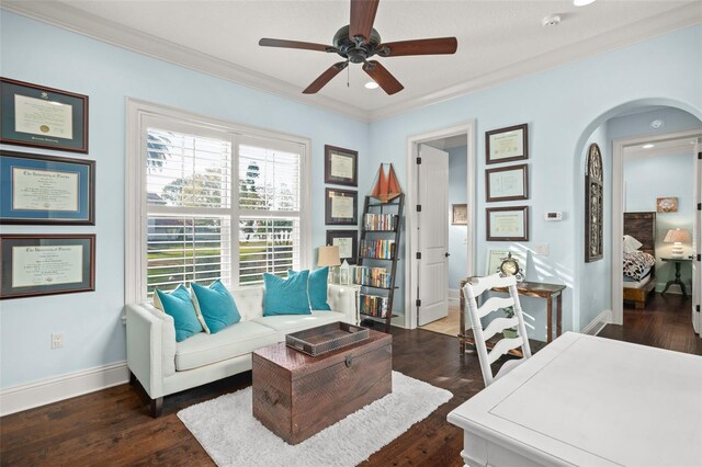 living area featuring arched walkways, dark wood-type flooring, a ceiling fan, baseboards, and ornamental molding