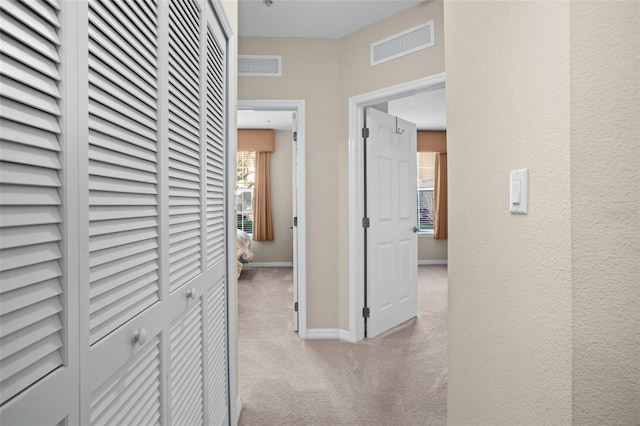 corridor featuring carpet floors, visible vents, a textured wall, and baseboards