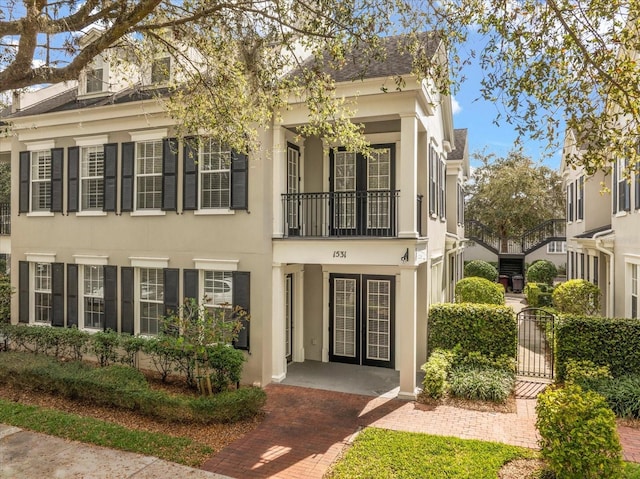 view of front facade with a gate, french doors, a balcony, and stucco siding