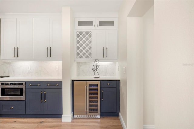 bar featuring light wood finished floors, tasteful backsplash, wine cooler, a bar, and stainless steel oven