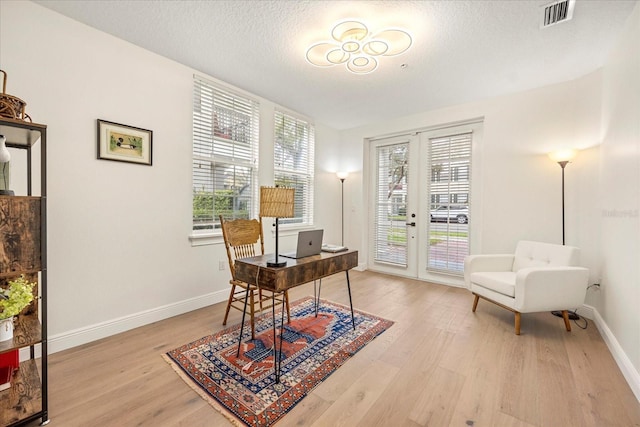 home office featuring a textured ceiling, french doors, visible vents, and light wood-style floors