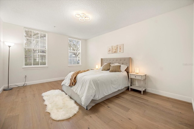 bedroom featuring light wood-style floors, baseboards, and a textured ceiling