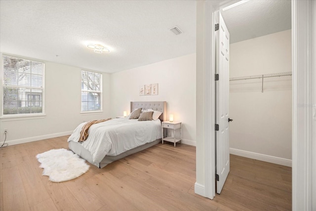 bedroom with light wood-style floors, visible vents, a textured ceiling, and baseboards