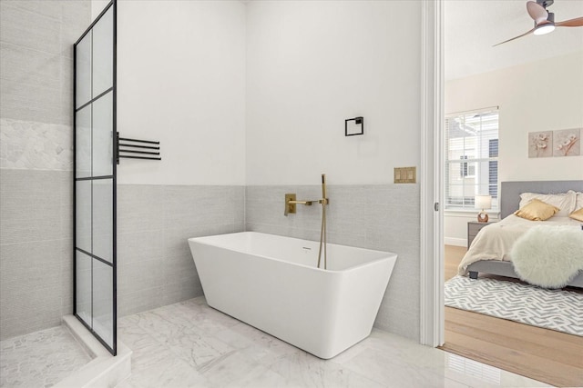 full bathroom with marble finish floor, tile walls, connected bathroom, a freestanding tub, and tiled shower