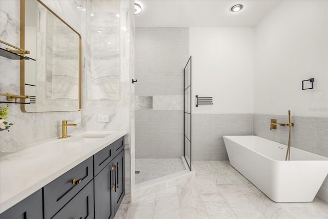 full bathroom featuring marble finish floor, tile walls, a tile shower, vanity, and a freestanding tub