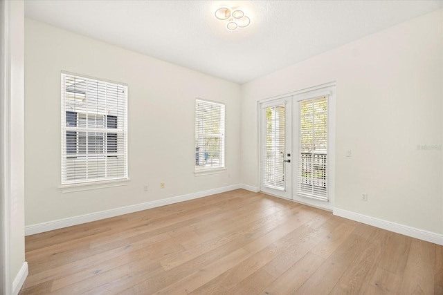 empty room featuring light wood finished floors, french doors, and baseboards