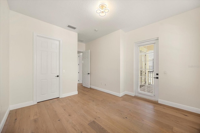 empty room with light wood-type flooring, visible vents, and baseboards