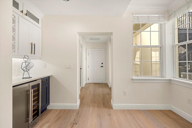 bar featuring light wood-type flooring, beverage cooler, visible vents, and baseboards