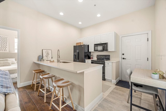 kitchen featuring a peninsula, a sink, white cabinets, black appliances, and a kitchen bar