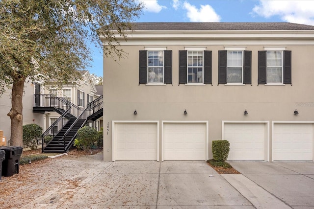 view of side of home featuring concrete driveway, stucco siding, an attached garage, and stairs