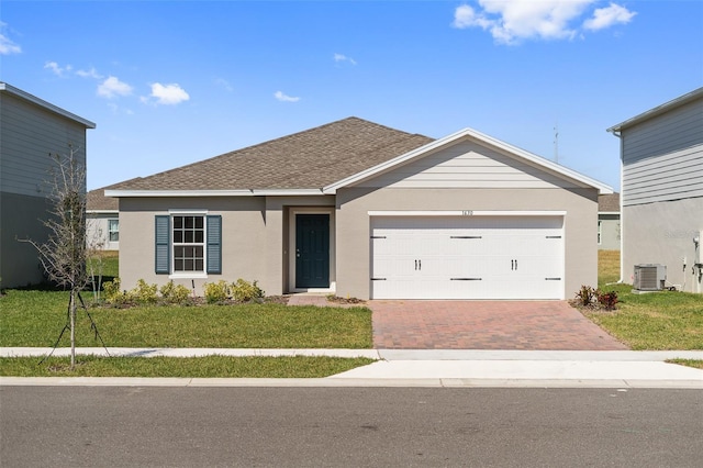 single story home featuring a garage, a shingled roof, decorative driveway, central AC, and a front yard