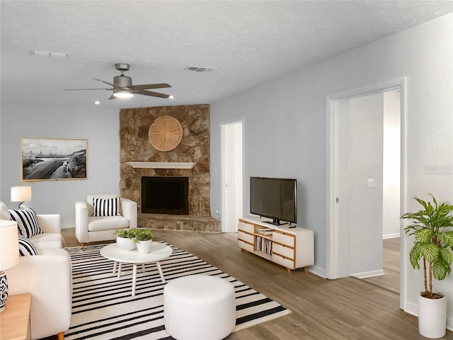 living area with visible vents, a ceiling fan, a stone fireplace, a textured ceiling, and wood finished floors