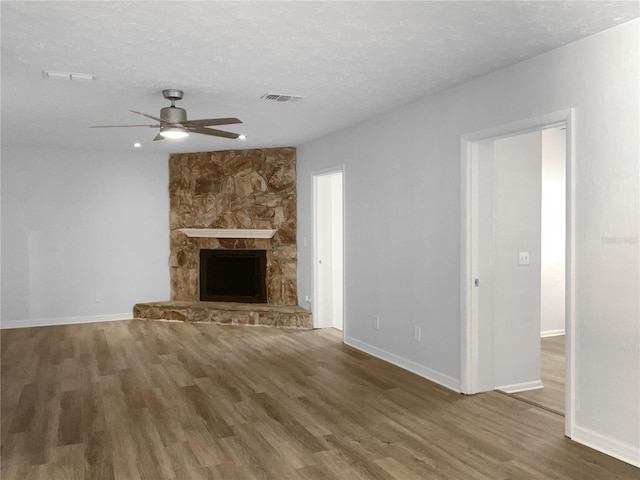 unfurnished living room featuring a fireplace, visible vents, a textured ceiling, wood finished floors, and baseboards