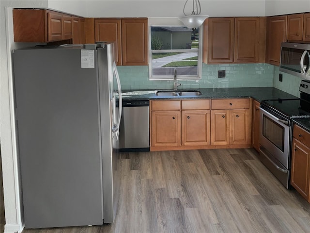 kitchen with stainless steel appliances, brown cabinetry, a sink, and light wood-style flooring