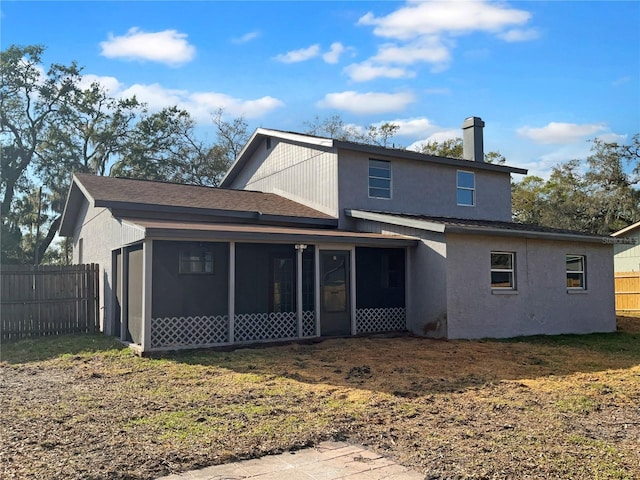 rear view of house with a sunroom, a chimney, fence, and stucco siding