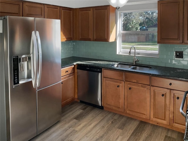 kitchen with light wood-style flooring, dark stone countertops, stainless steel appliances, and a sink