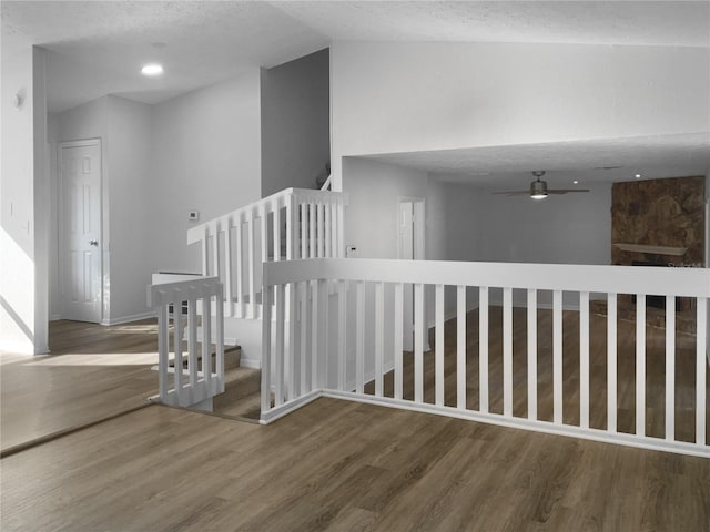 stairway with a ceiling fan, vaulted ceiling, a textured ceiling, and wood finished floors