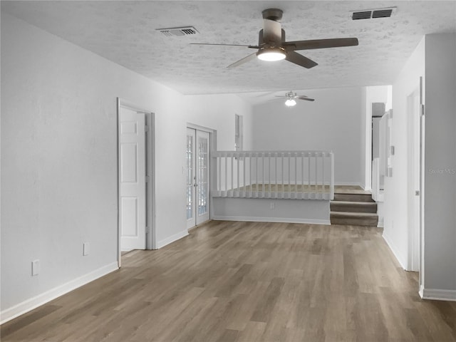 empty room featuring a textured ceiling, stairs, wood finished floors, and visible vents