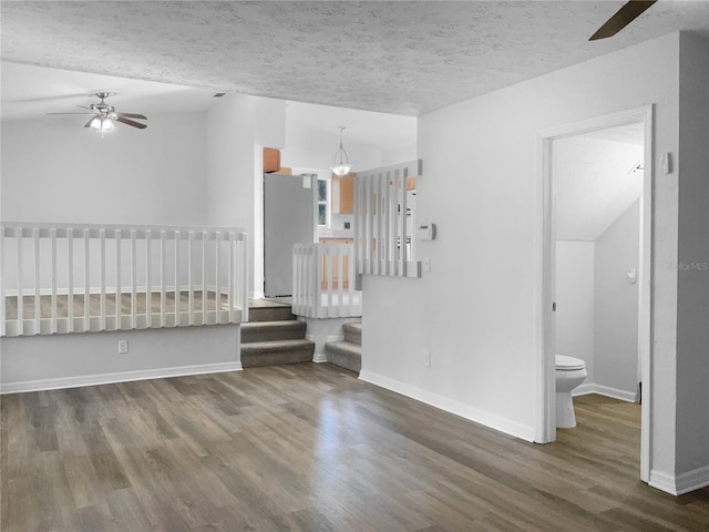 empty room with baseboards, a ceiling fan, wood finished floors, stairs, and a textured ceiling