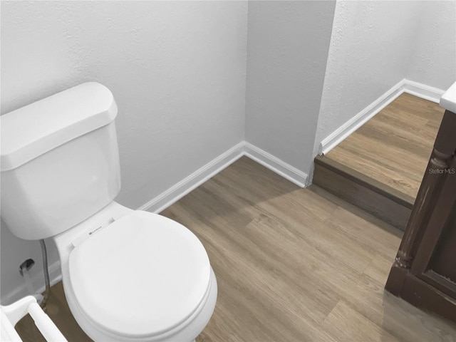 bathroom featuring a textured wall, wood finished floors, toilet, and baseboards