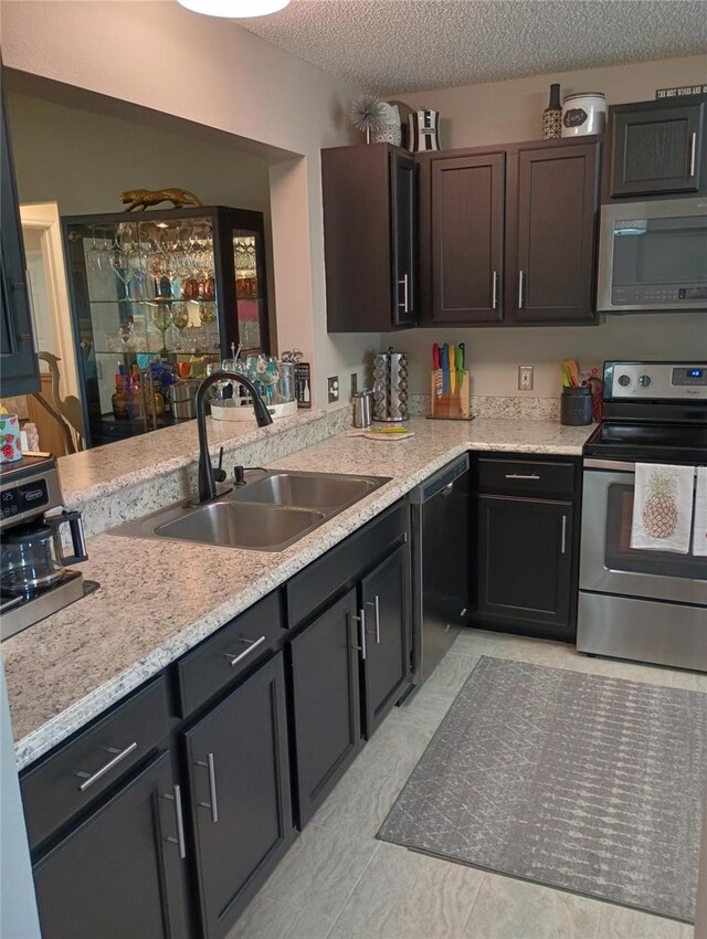 kitchen with a textured ceiling, stainless steel appliances, a sink, and dark brown cabinetry