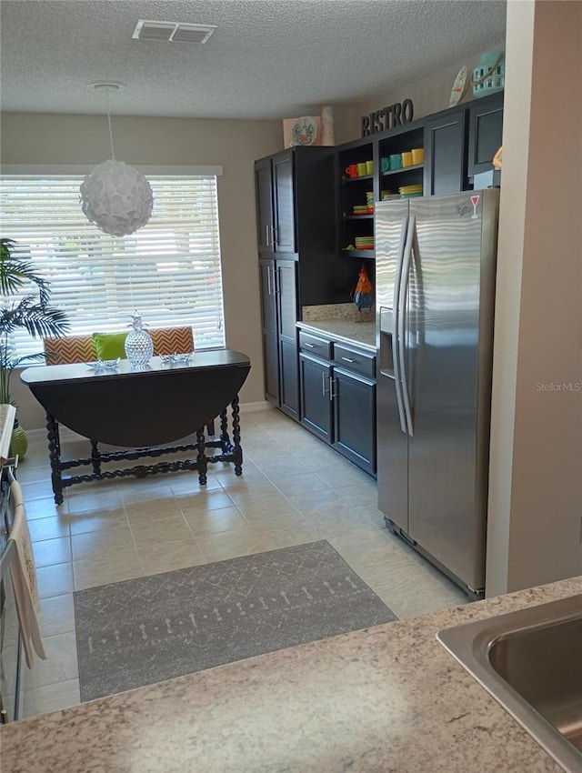 kitchen featuring stainless steel fridge, visible vents, decorative light fixtures, a textured ceiling, and a sink