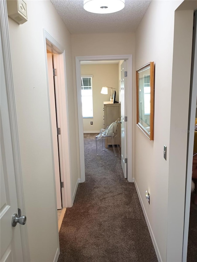 hall with a textured ceiling, carpet, and baseboards