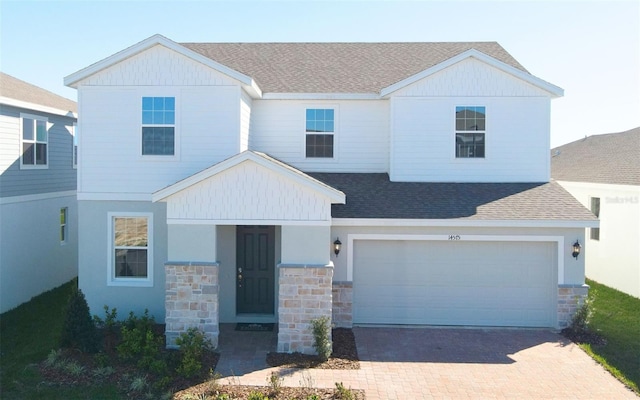 view of front facade featuring decorative driveway, stone siding, an attached garage, and a shingled roof