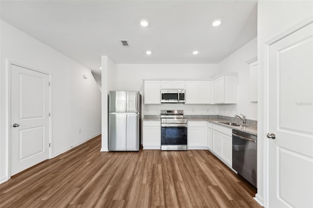 kitchen with wood finished floors, a sink, white cabinets, appliances with stainless steel finishes, and light stone countertops