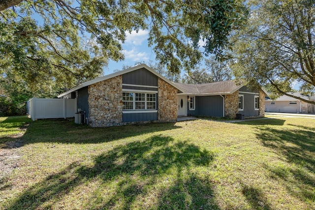 mid-century home with stone siding, a front lawn, and fence