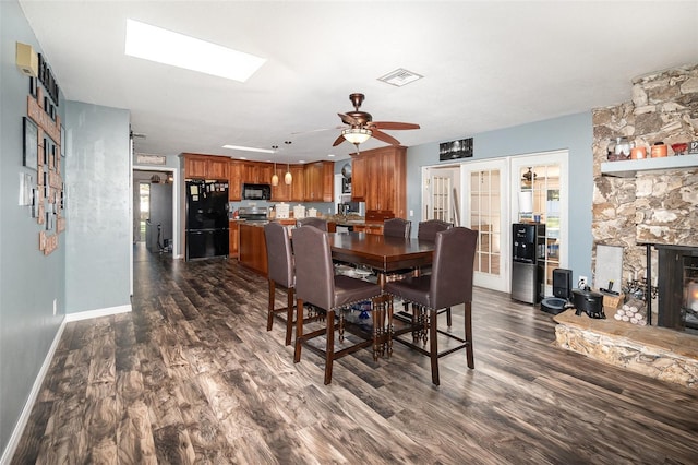 dining area with ceiling fan, a stone fireplace, dark wood-type flooring, visible vents, and baseboards