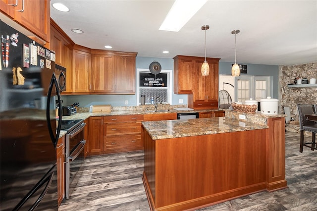 kitchen featuring a skylight, a sink, light stone countertops, black appliances, and brown cabinetry