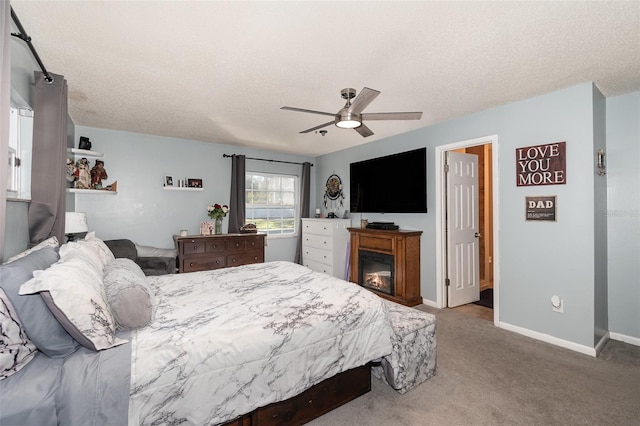 carpeted bedroom with a glass covered fireplace, ceiling fan, a textured ceiling, and baseboards