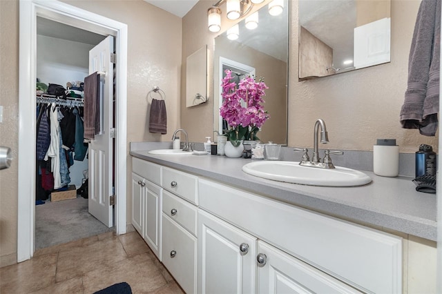 bathroom featuring a textured wall, a spacious closet, double vanity, and a sink