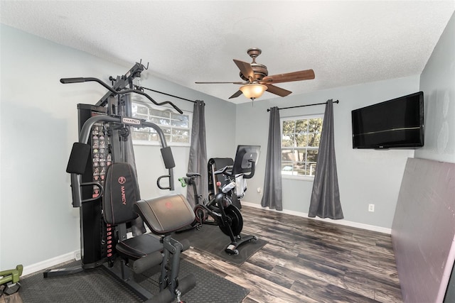 workout room with ceiling fan, a textured ceiling, baseboards, and wood finished floors