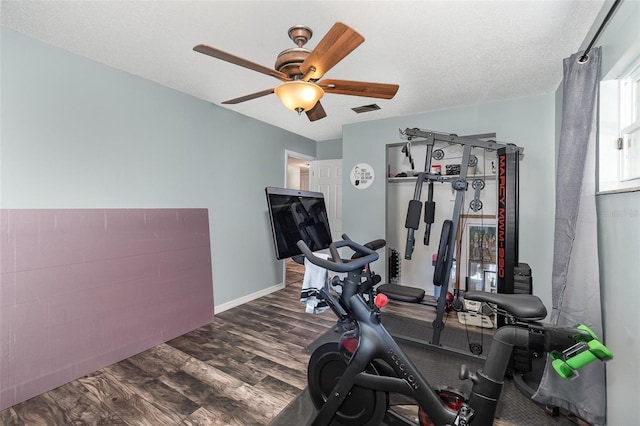 exercise area featuring ceiling fan, a textured ceiling, wood finished floors, visible vents, and baseboards