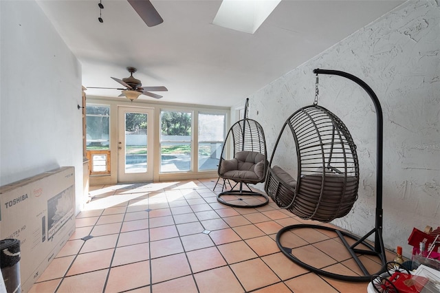 unfurnished room featuring ceiling fan, a textured wall, a skylight, and light tile patterned flooring