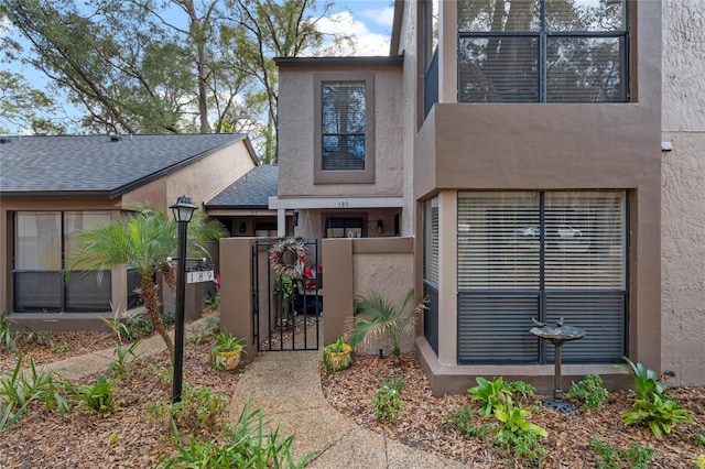 entrance to property with a gate, fence, and stucco siding