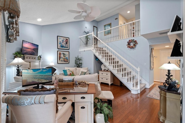 living room featuring hardwood / wood-style flooring, a high ceiling, visible vents, a ceiling fan, and stairs