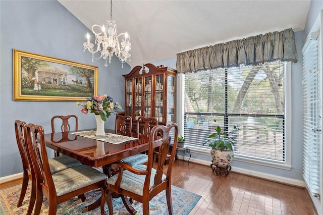 dining space with lofted ceiling, a chandelier, hardwood / wood-style flooring, and baseboards