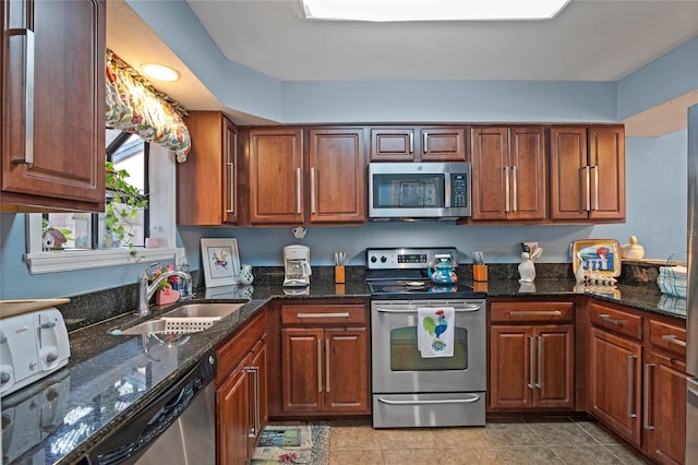 kitchen with appliances with stainless steel finishes, brown cabinetry, a sink, dark stone counters, and tile patterned floors