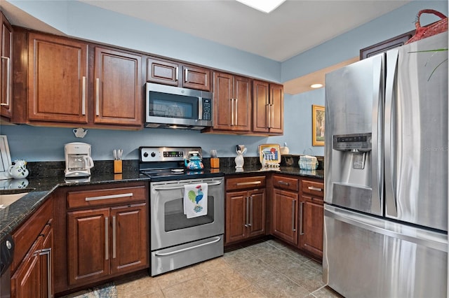 kitchen with dark stone counters, stainless steel appliances, light tile patterned floors, and brown cabinetry