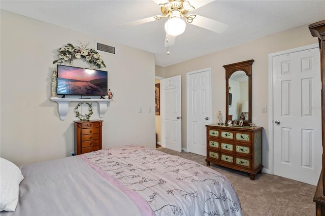 carpeted bedroom with a textured ceiling, visible vents, and a ceiling fan