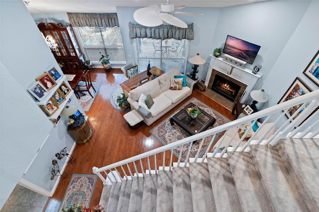 living area with wood finished floors, a ceiling fan, baseboards, stairway, and a tiled fireplace