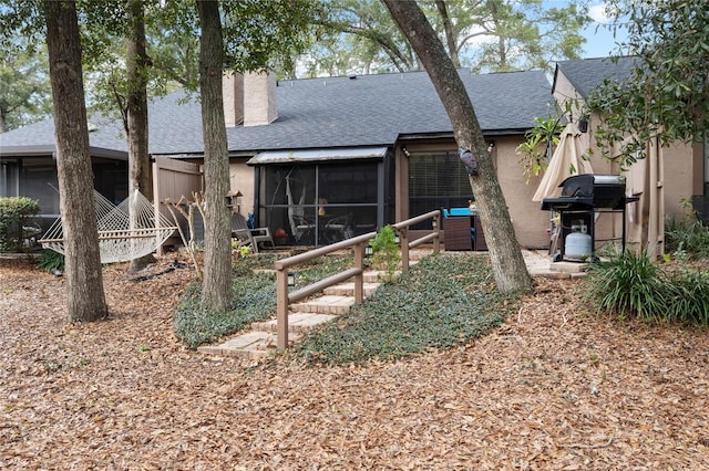 back of house with a sunroom, roof with shingles, a chimney, and stucco siding